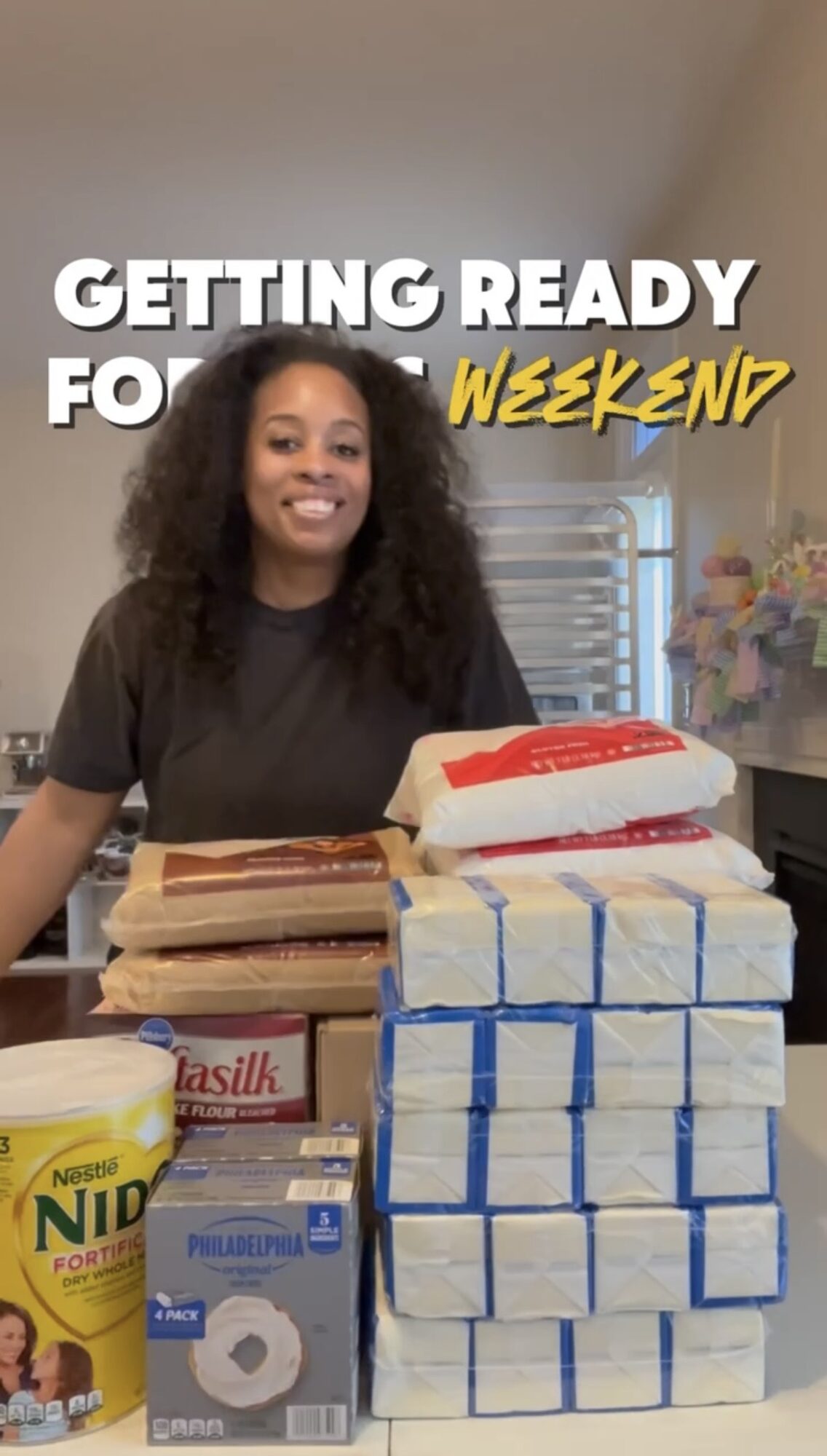 Woman smiling behind stacks of paper towels and cleaning supplies in a room with flowers and a window.