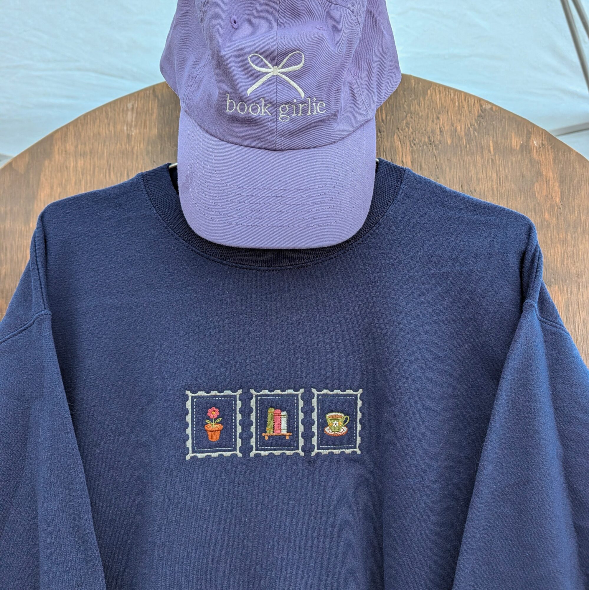 Person wearing a purple cap and navy blue sweatshirt with three small postage stamp designs, on a wooden surface.